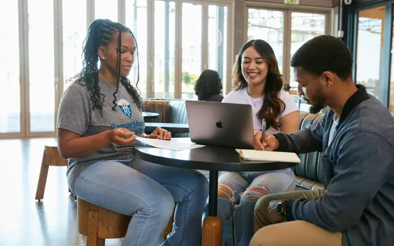Three students in street clothes studying at a cafe